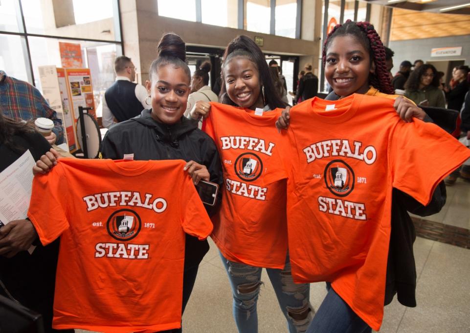 Three students holding up orange Buffalo State T-shirts
